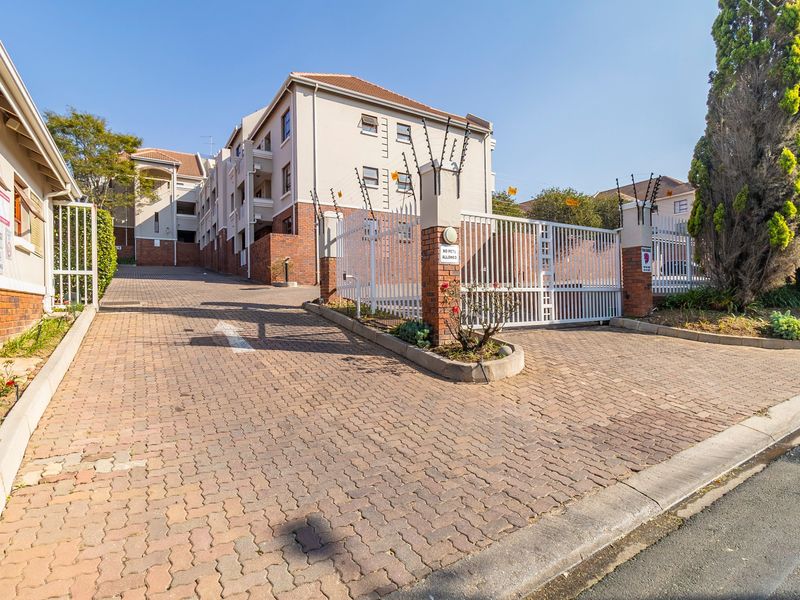 Front entrance view of an apartment complex featuring a paved driveway, secure gated access, and perimeter electric fencing.