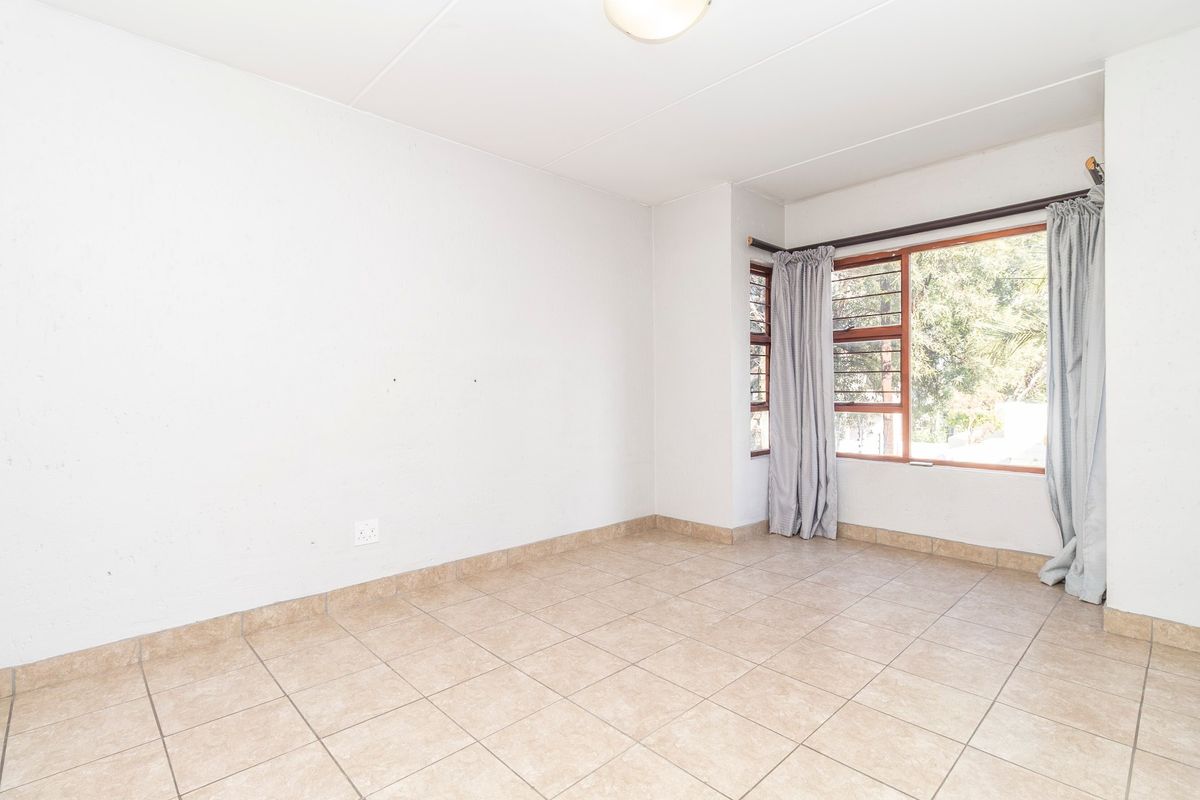 A bright, empty bedroom featuring neutral tiled flooring and large timber-framed windows with security bars, offering a clean canvas for personalization.