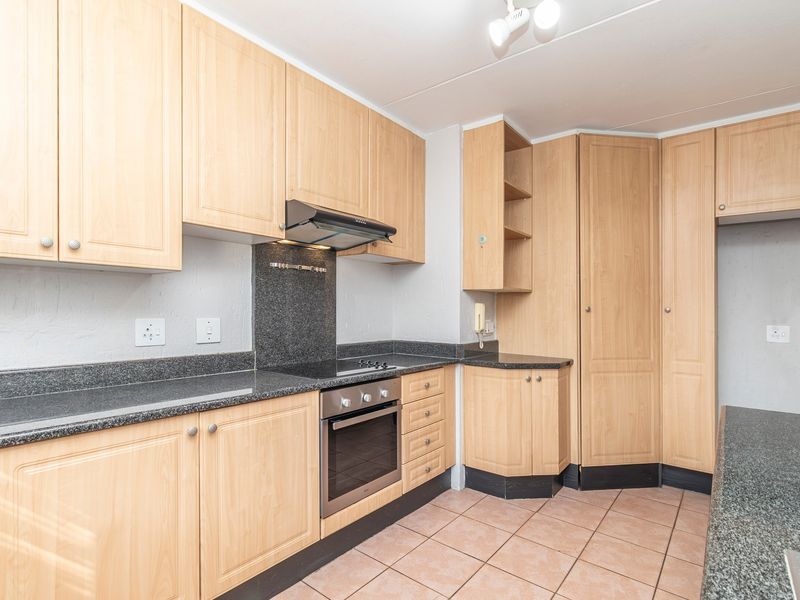 A functional kitchen featuring light wood laminate cabinetry, granite countertops, built-in oven, and electric hob with an extractor fan.