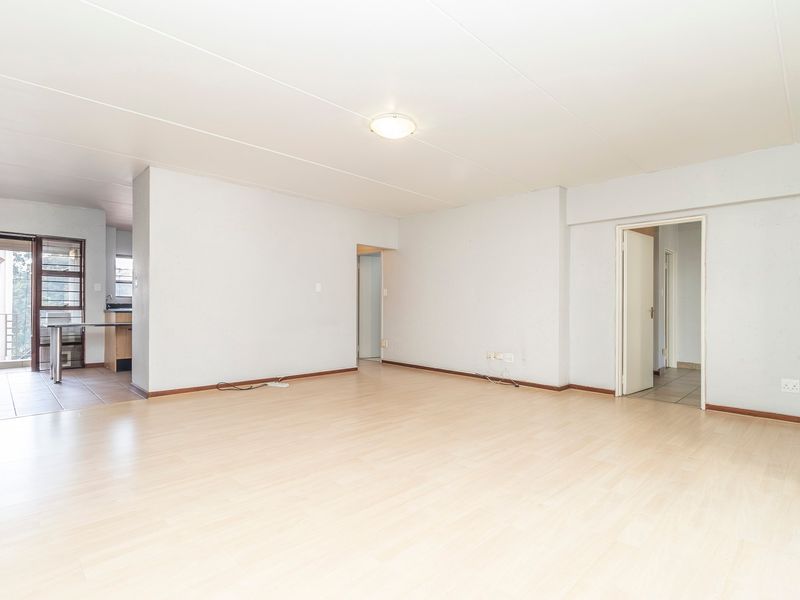 Spacious open-plan living area featuring light laminate flooring, neutral walls, and direct access to an adjoining kitchen and balcony area.