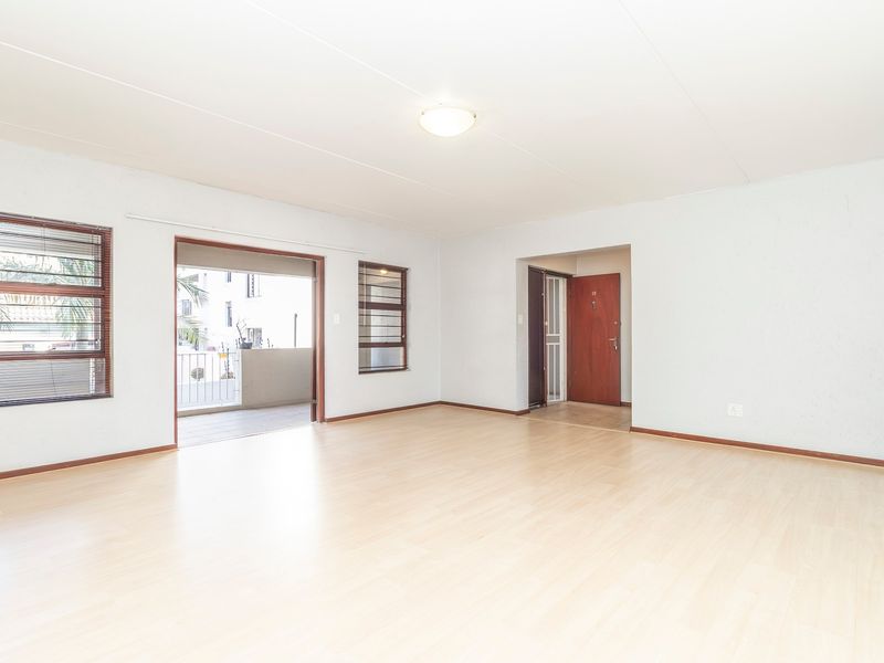 Spacious, light-filled living area featuring neutral walls, laminate flooring, and direct access to an outdoor balcony through a sliding door.