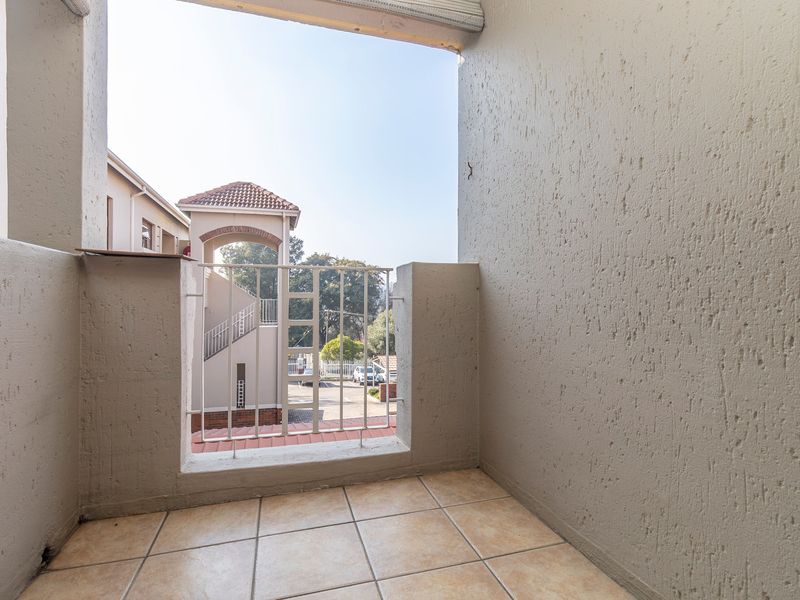 A compact balcony featuring tiled flooring and a metal balustrade, offering an open view of the apartment complex grounds.