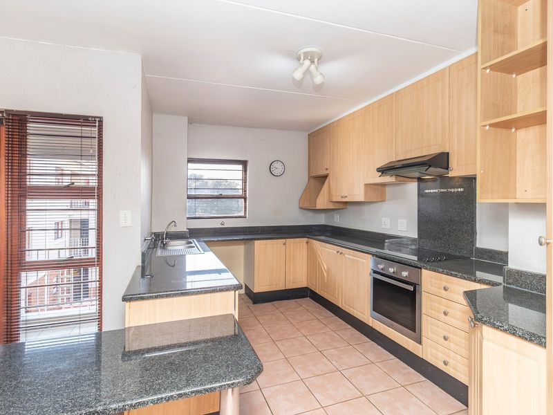 A functional kitchen featuring light wood cabinetry, granite countertops, built-in oven, hob, and extractor fan, with tiled flooring and direct access to a balcony.