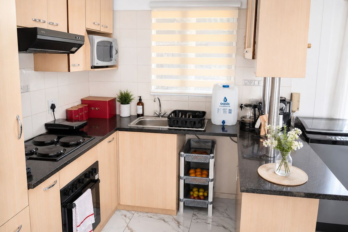 A functional kitchen featuring light wood cabinetry, dark granite countertops, integrated appliances, and modern marble-look floor tiles.
