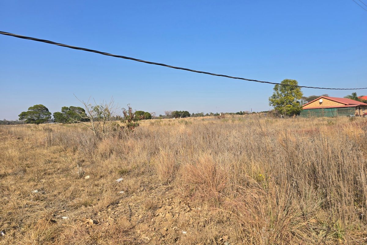 A view of a vacant residential plot featuring dry grass and overhead power lines with neighboring property visible in the distance.