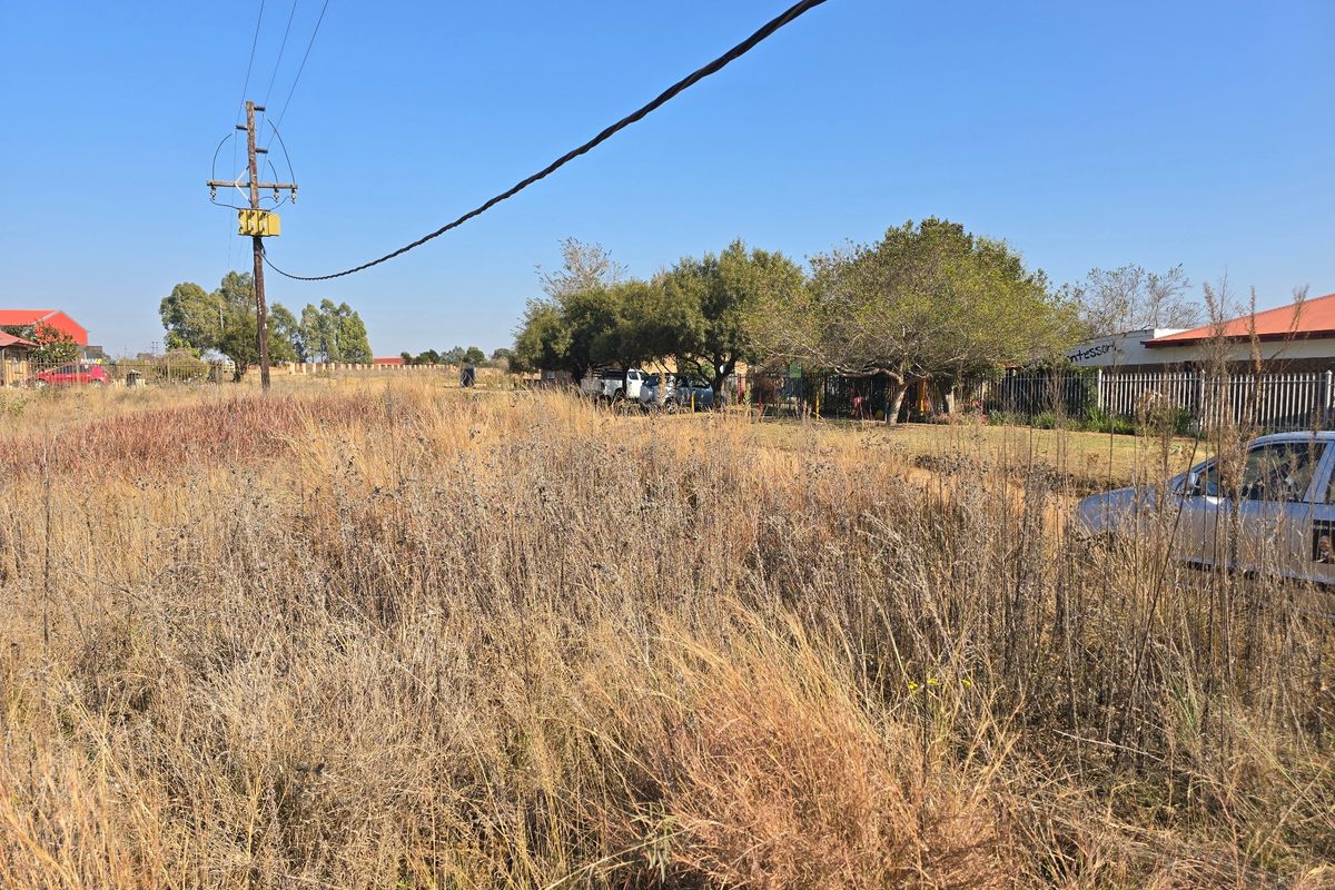 A vacant residential plot featuring overgrown grass, a utility pole with overhead power lines, and perimeter fencing.
