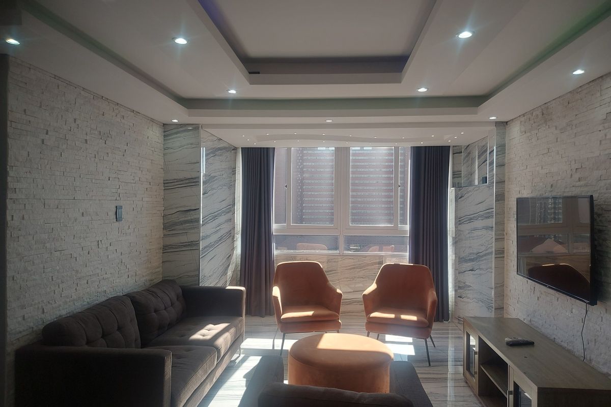Modern living room featuring a stone-clad feature wall, marble flooring, recessed ceiling with downlights, and large windows with city views.