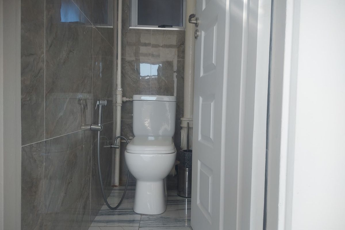 A compact bathroom featuring modern grey wall tiles, marble-effect floor tiles, and a standard white toilet with a bidet spray attachment.