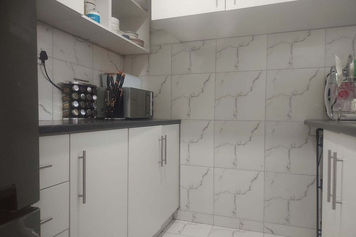 A compact, modern kitchen featuring white cabinetry, marble-effect wall and floor tiling, and dark countertops.