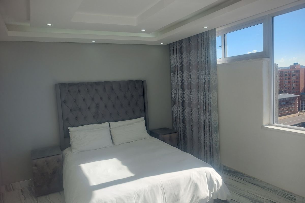A well-lit bedroom featuring a tray ceiling with recessed lighting and modern marble-look floor tiles, offering a bright and contemporary living space.