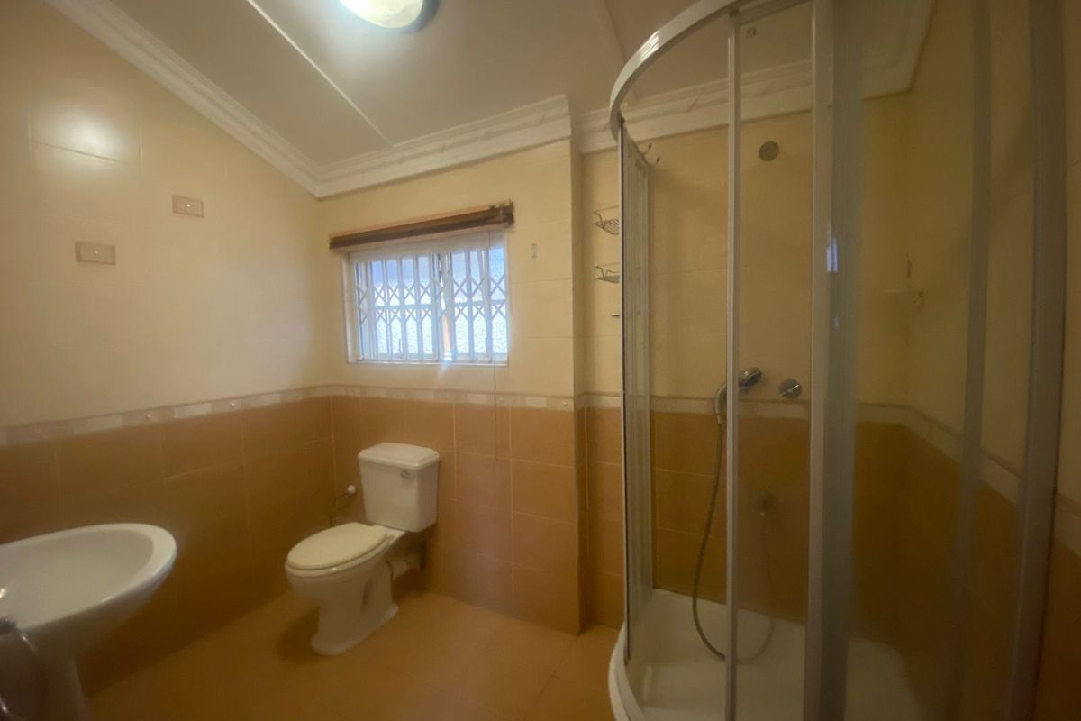 A functional bathroom featuring a corner shower enclosure, pedestal basin, and toilet with neutral wall and floor tiling.