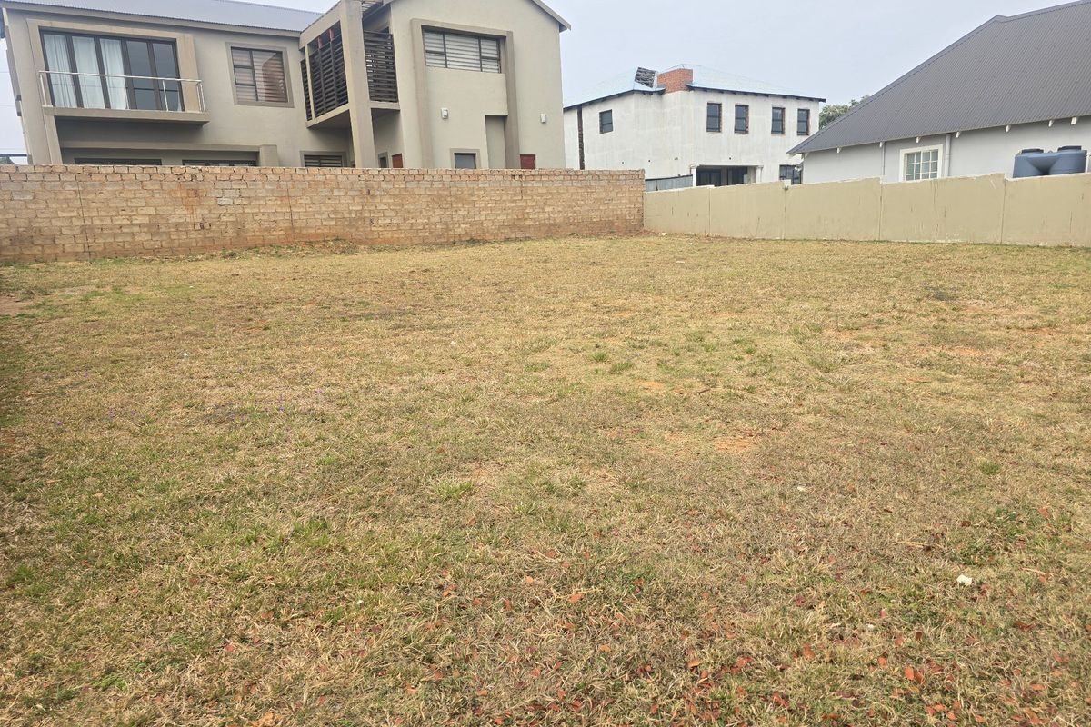A vacant residential plot featuring a grass lawn and perimeter boundary walls, situated in a developed neighborhood.