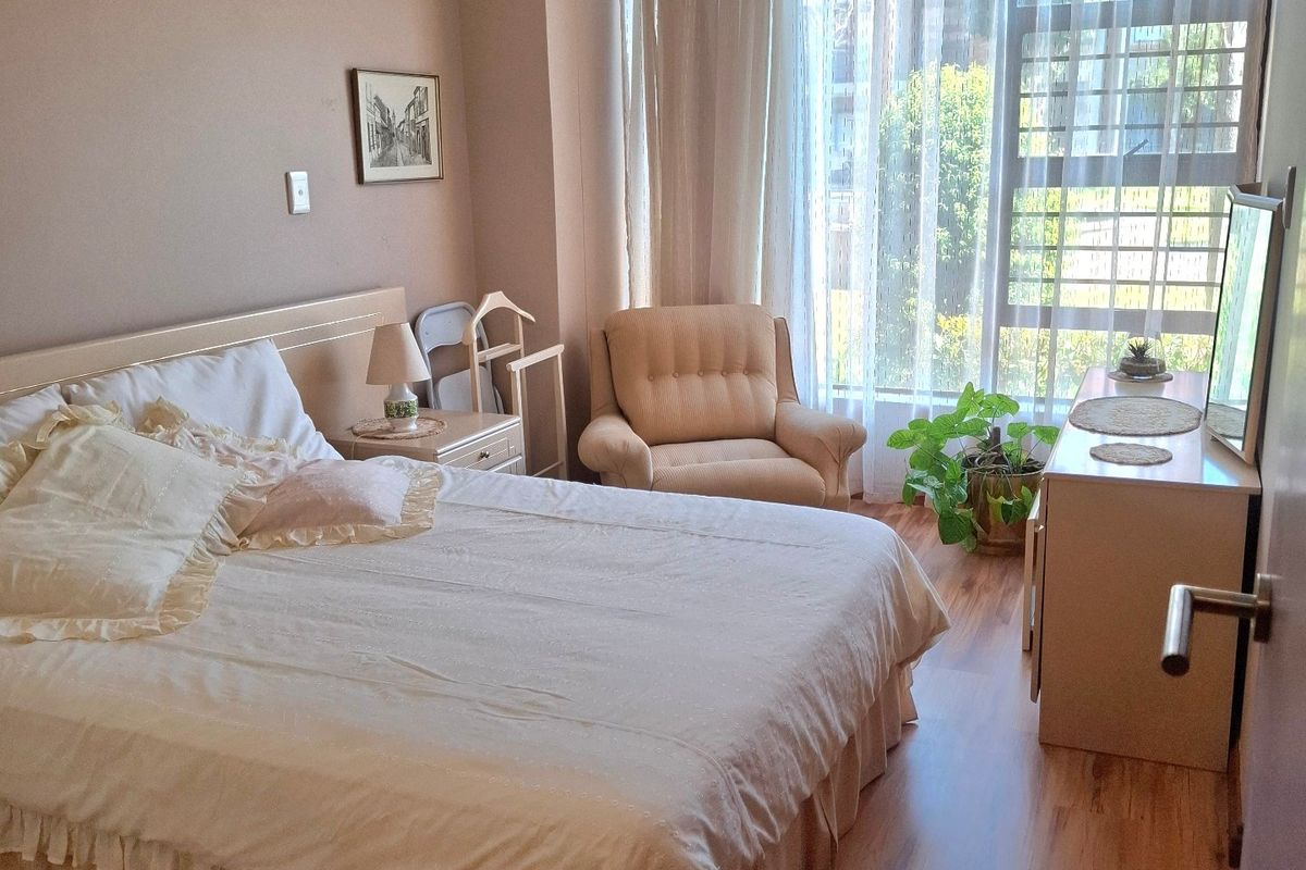 A well-lit bedroom featuring laminate flooring, neutral wall tones, and a large floor-to-ceiling window that provides ample natural light.