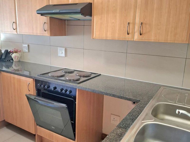 Functional kitchen featuring laminate cabinetry, granite countertops, built-in oven with hob, extractor fan, and a double bowl stainless steel sink.