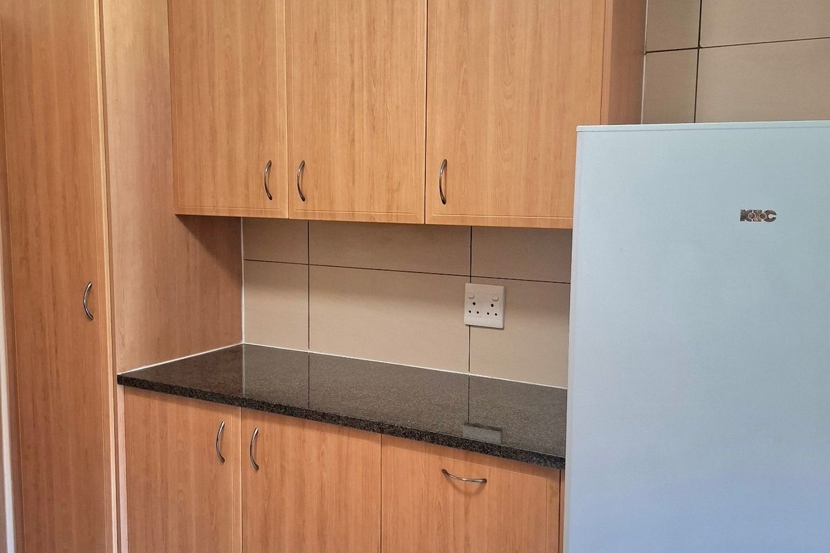 A functional kitchen area featuring light wood-tone cabinetry, dark granite countertops, and neutral tiled backsplash and flooring.