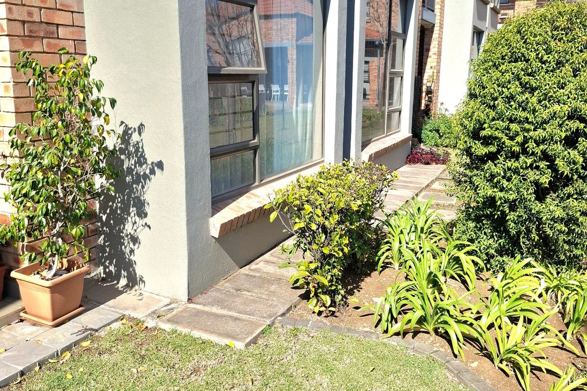 A well-maintained rear exterior view of the apartment featuring a brick and rendered facade, large aluminium windows, and a landscaped garden area.