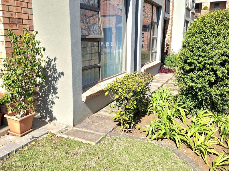 A well-maintained rear exterior view of the apartment featuring a brick and rendered facade, large aluminium windows, and a landscaped garden area.
