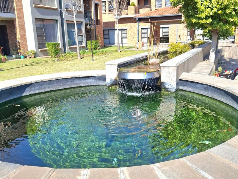 A well-maintained communal garden area featuring a decorative circular water fountain and brick apartment building facades in the background.