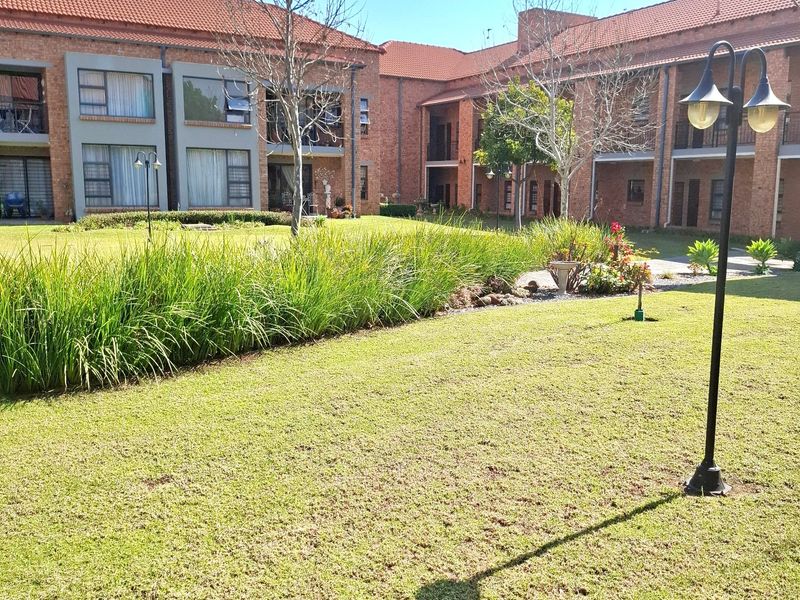 A well-maintained communal garden area featuring manicured lawns and established landscaping, set against the brick facade of the apartment complex.