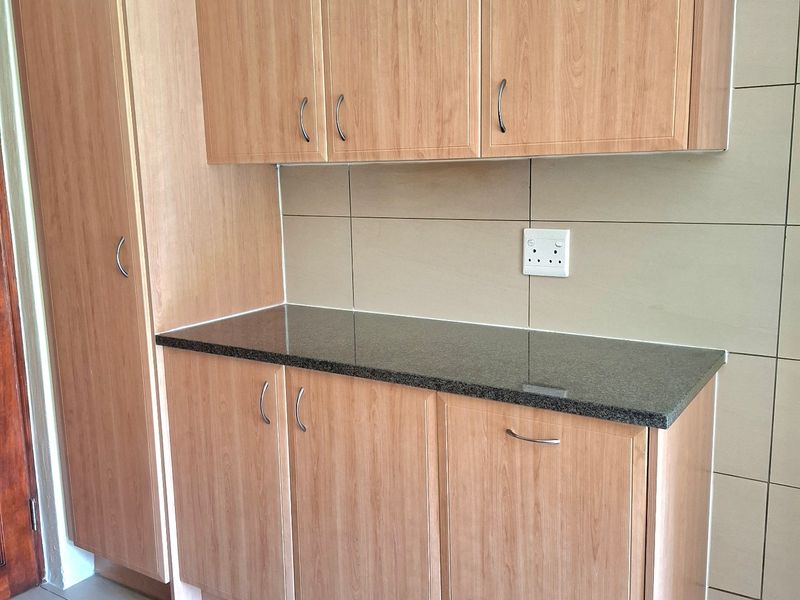 A clean, functional kitchen area featuring light wood-finish cabinetry, a dark granite countertop, and neutral tiled walls and flooring.
