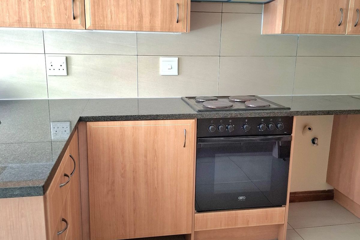 A clean, functional kitchen featuring light wood-finish cabinetry, granite countertops, and a built-in oven with an electric hob and extractor fan.