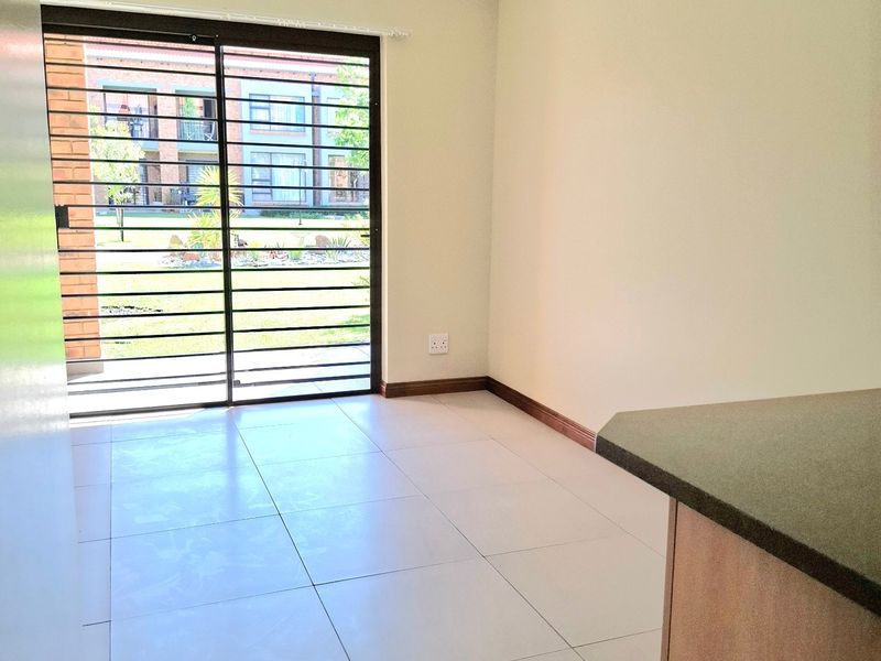 An empty open-plan living area featuring neutral tiled flooring, a ceiling light, and a sliding glass door with security bars leading to the exterior.