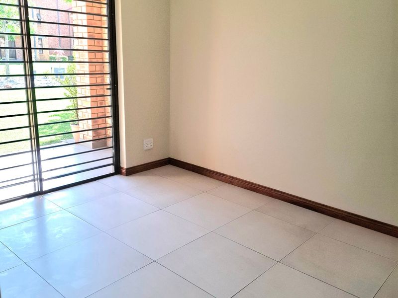A bright, empty living area featuring neutral tiled flooring, skirting boards, and a sliding glass door with an integrated security gate leading outdoors.