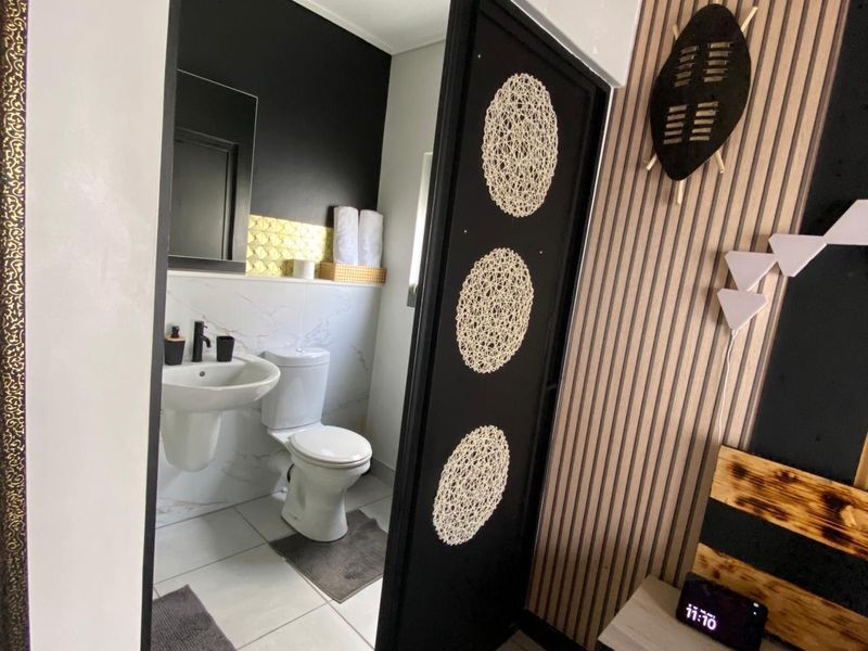A modern bathroom featuring a pedestal basin and toilet, accessed via a sliding door from the adjacent bedroom area.