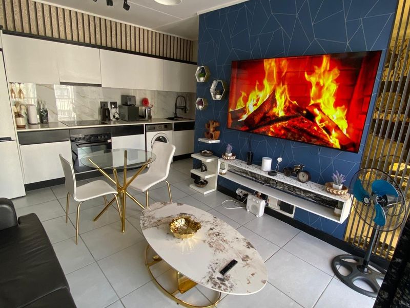 Modern open-plan living area featuring a compact kitchen with built-in cabinetry, integrated appliances, and a stylish feature wall with built-in shelving.
