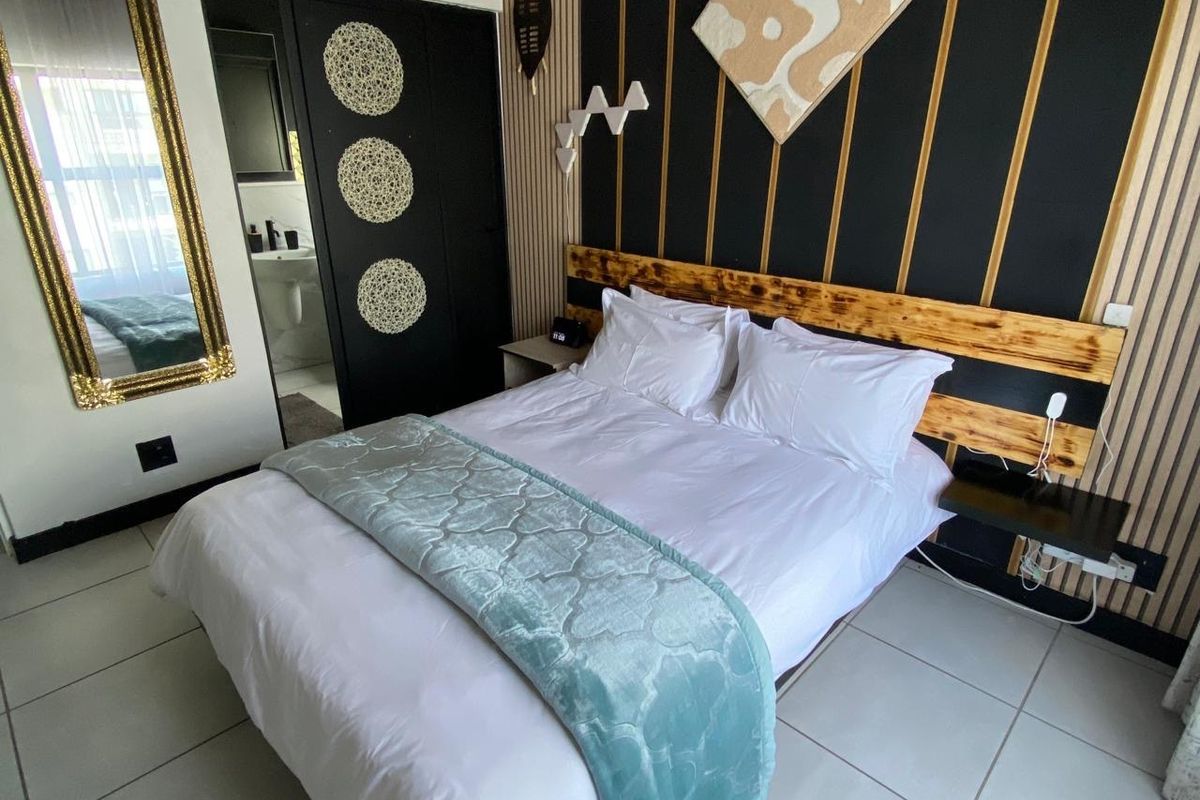 A well-maintained bedroom featuring modern slatted wood wall paneling, a built-in headboard, tiled flooring, and direct access to an en-suite bathroom.