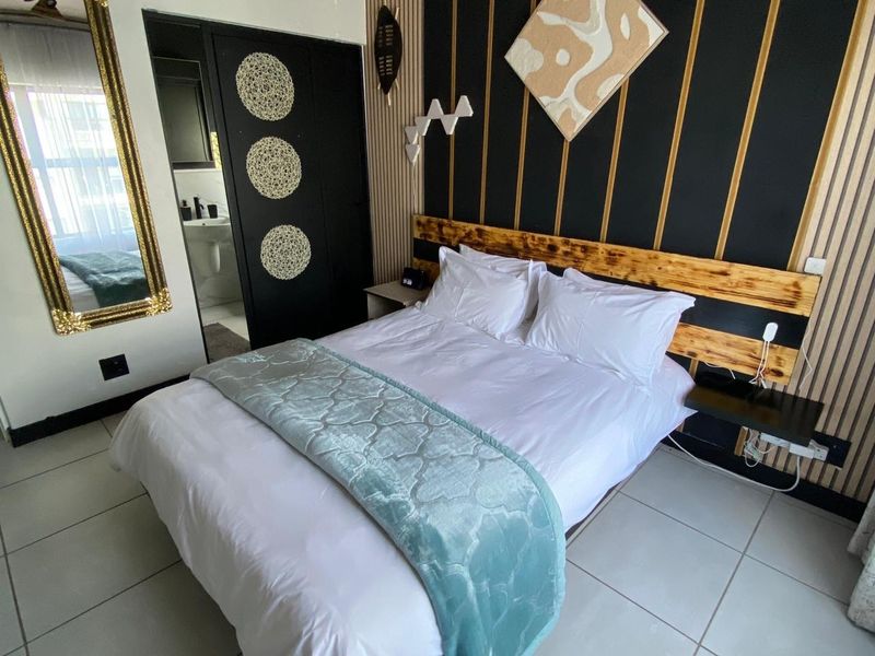A well-maintained bedroom featuring modern slatted wood wall paneling, a built-in headboard, tiled flooring, and direct access to an en-suite bathroom.