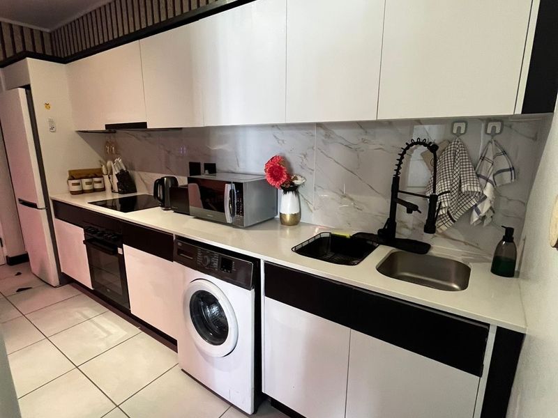 Modern galley-style kitchen featuring sleek white and black cabinetry, marble-look backsplash, integrated oven, hob, and a contemporary gooseneck faucet.