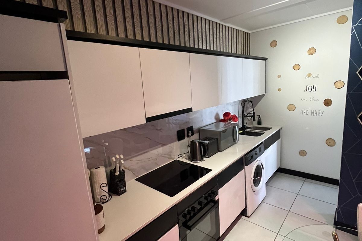 Modern kitchen featuring sleek white cabinetry, integrated appliances including an oven and washing machine, tiled flooring, and contemporary track lighting.