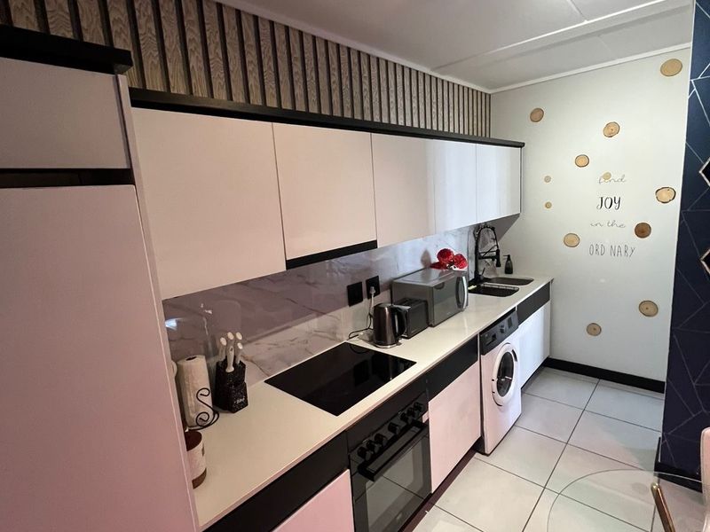 Modern kitchen featuring sleek white cabinetry, integrated appliances including an oven and washing machine, tiled flooring, and contemporary track lighting.