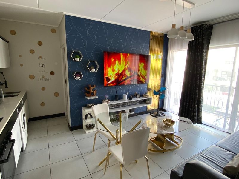 Modern open-plan living area featuring tiled floors, a feature wall with built-in shelving, and direct access to a balcony through sliding glass doors.
