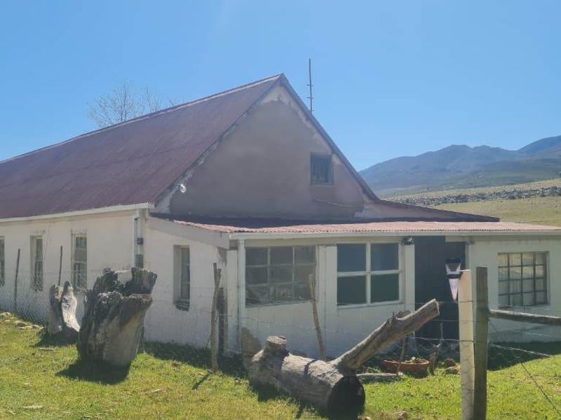 Rear view of a rural farmhouse featuring a corrugated metal roof and plastered masonry walls, set against a scenic mountain landscape.