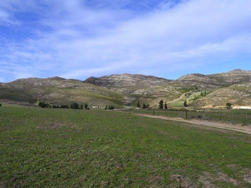 Expansive view of open farmland and rolling hills under a clear blue sky, featuring a dirt access track and perimeter wire fencing.