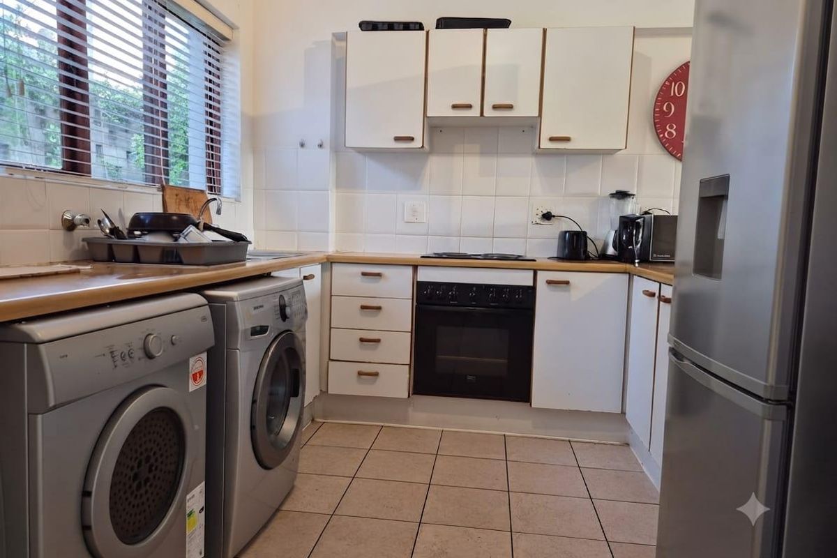 Functional kitchen featuring white cabinetry, tiled backsplash, built-in electric oven and hob, and tiled flooring with integrated laundry appliance connections.