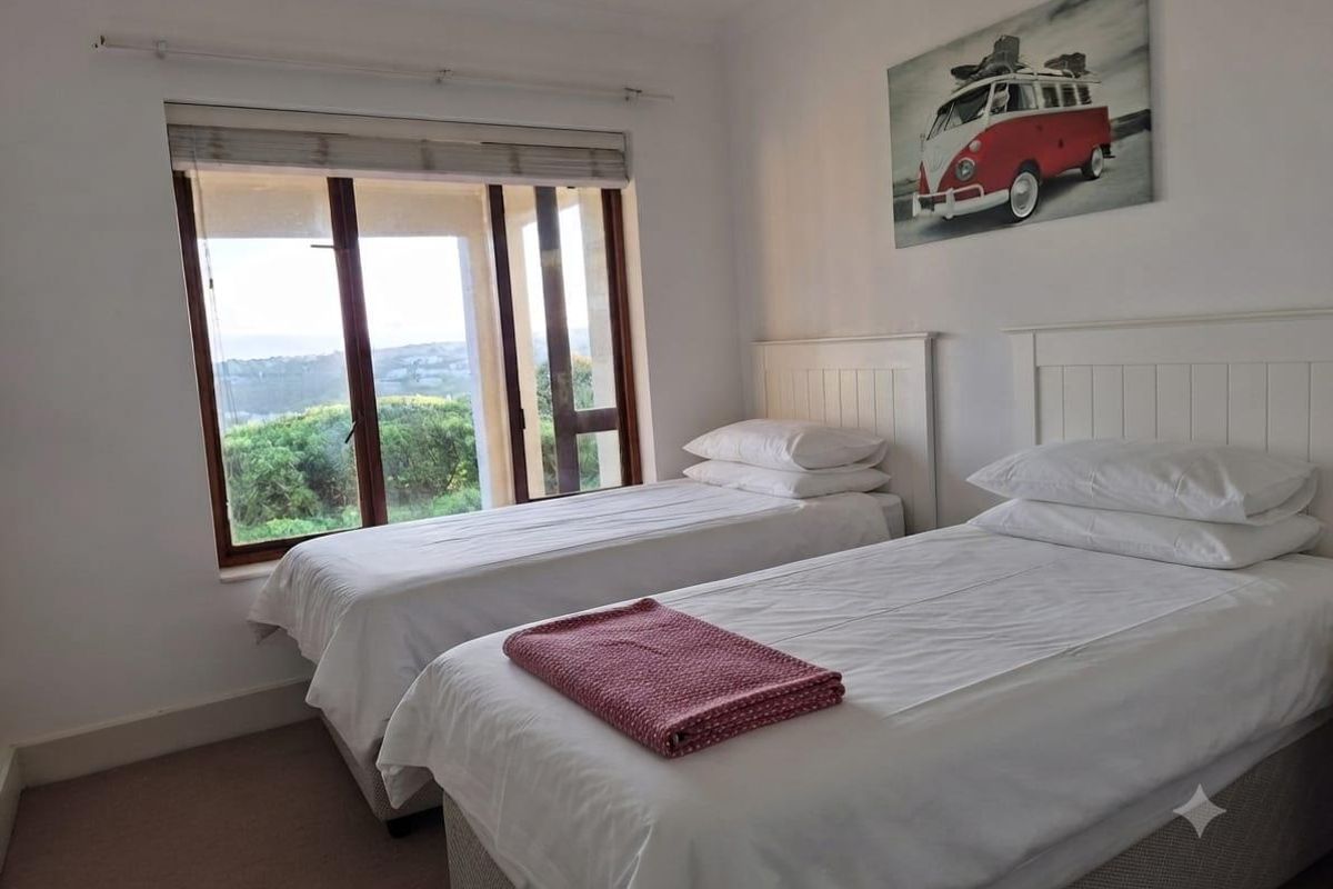 A bedroom featuring twin beds, carpeted flooring, and large timber-framed windows offering natural light and exterior views.