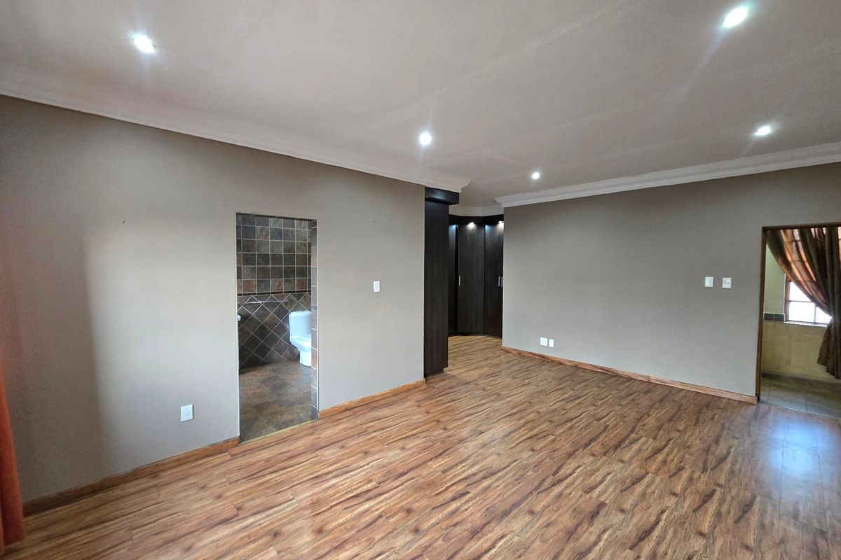 Spacious bedroom featuring laminate flooring, recessed downlighting, built-in cupboards, and direct access to an en-suite bathroom.