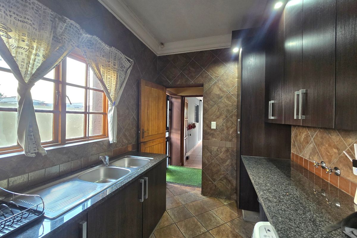 A functional kitchen featuring dark wood cabinetry, granite countertops, a double bowl stainless steel sink, and tiled finishes throughout.