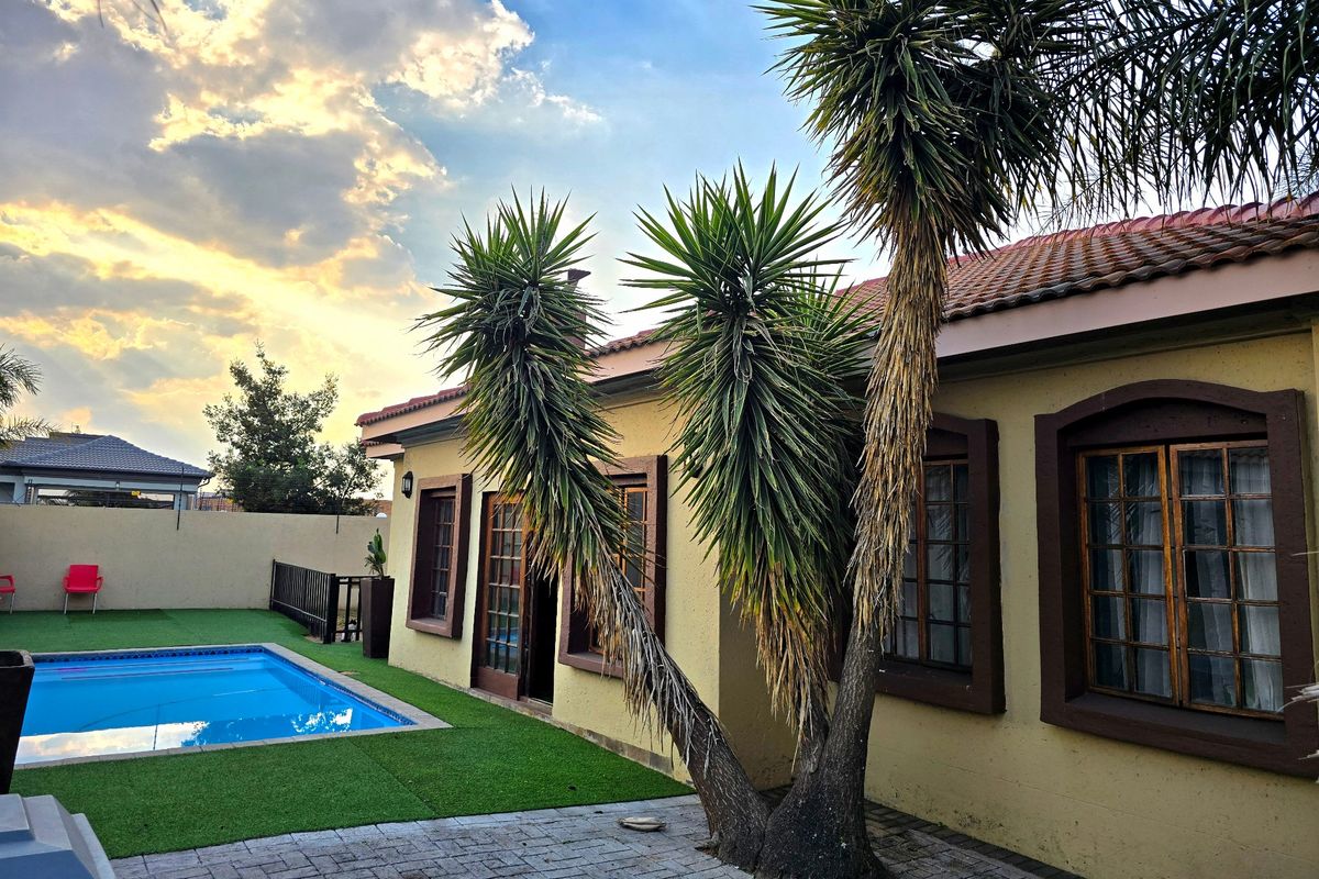 Rear exterior view of the townhouse featuring a swimming pool, paved patio area, artificial lawn, and established garden trees.