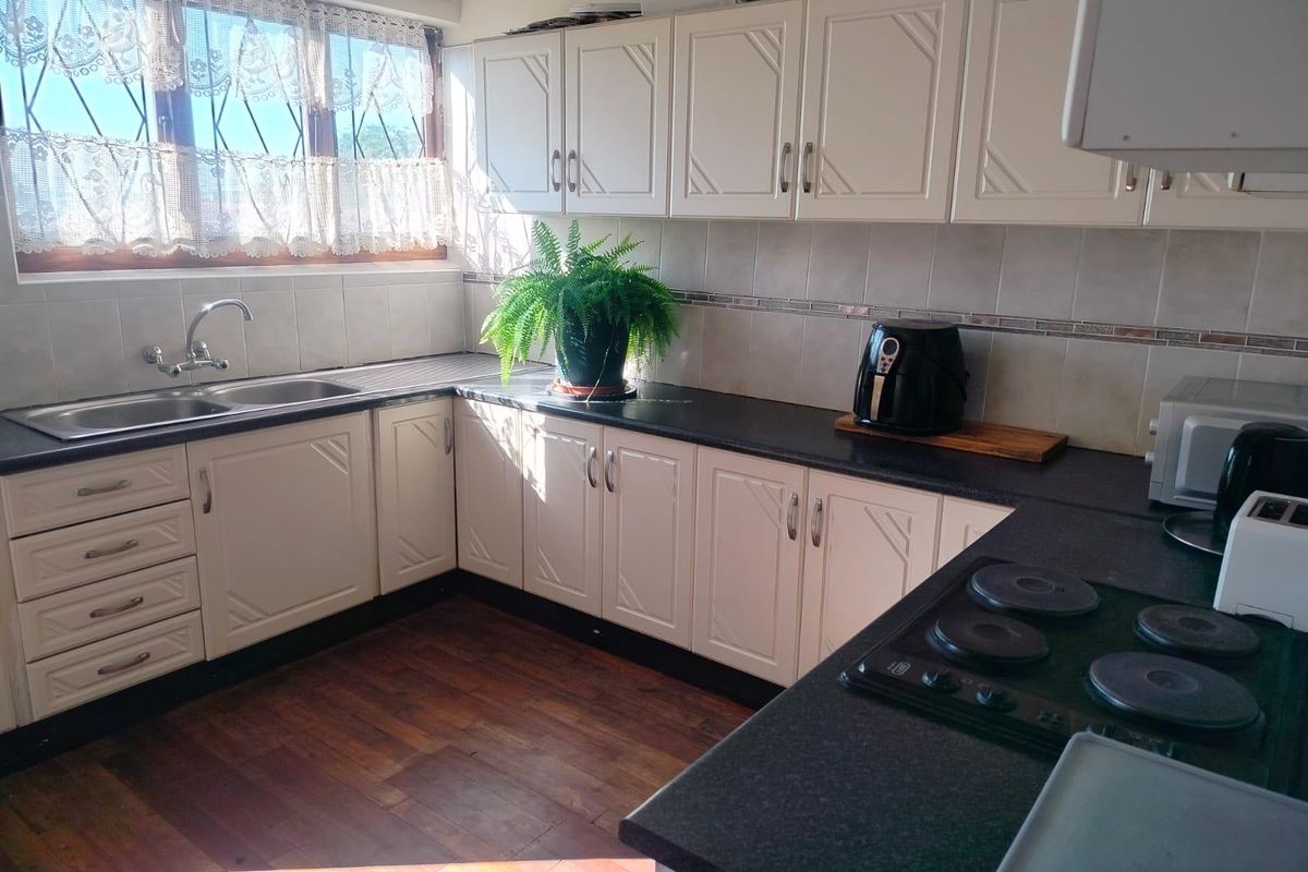 A functional kitchen featuring white cabinetry, dark laminate countertops, a stainless steel double sink, and an electric hob with tiled backsplash.