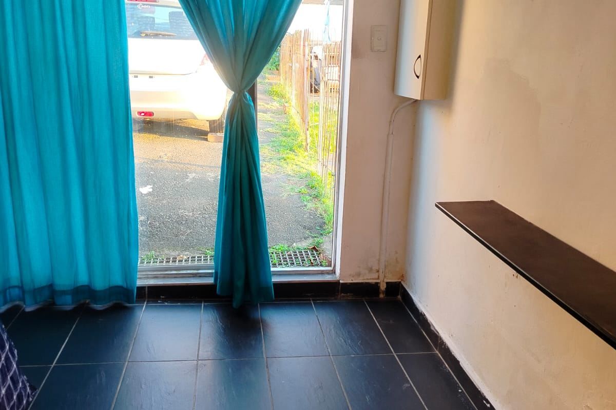 A small, empty living area featuring dark tiled flooring, a sliding glass door with curtains, and a wall-mounted shelf.