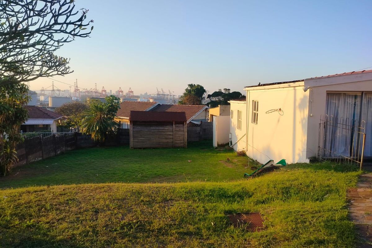 A spacious rear garden featuring a lawn, boundary wall, and a timber storage shed, with views of the surrounding area.
