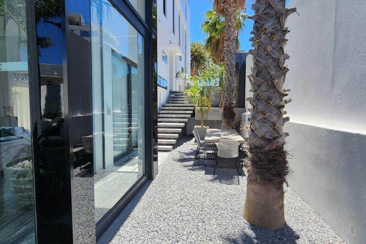A modern rear exterior space featuring large glass sliding doors, a gravel courtyard, and a concrete staircase leading to an upper level.