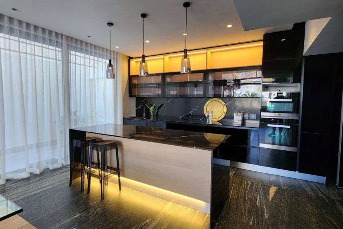 Modern kitchen featuring a sleek island, high-end built-in appliances, dark stone countertops, and sophisticated under-cabinet lighting.
