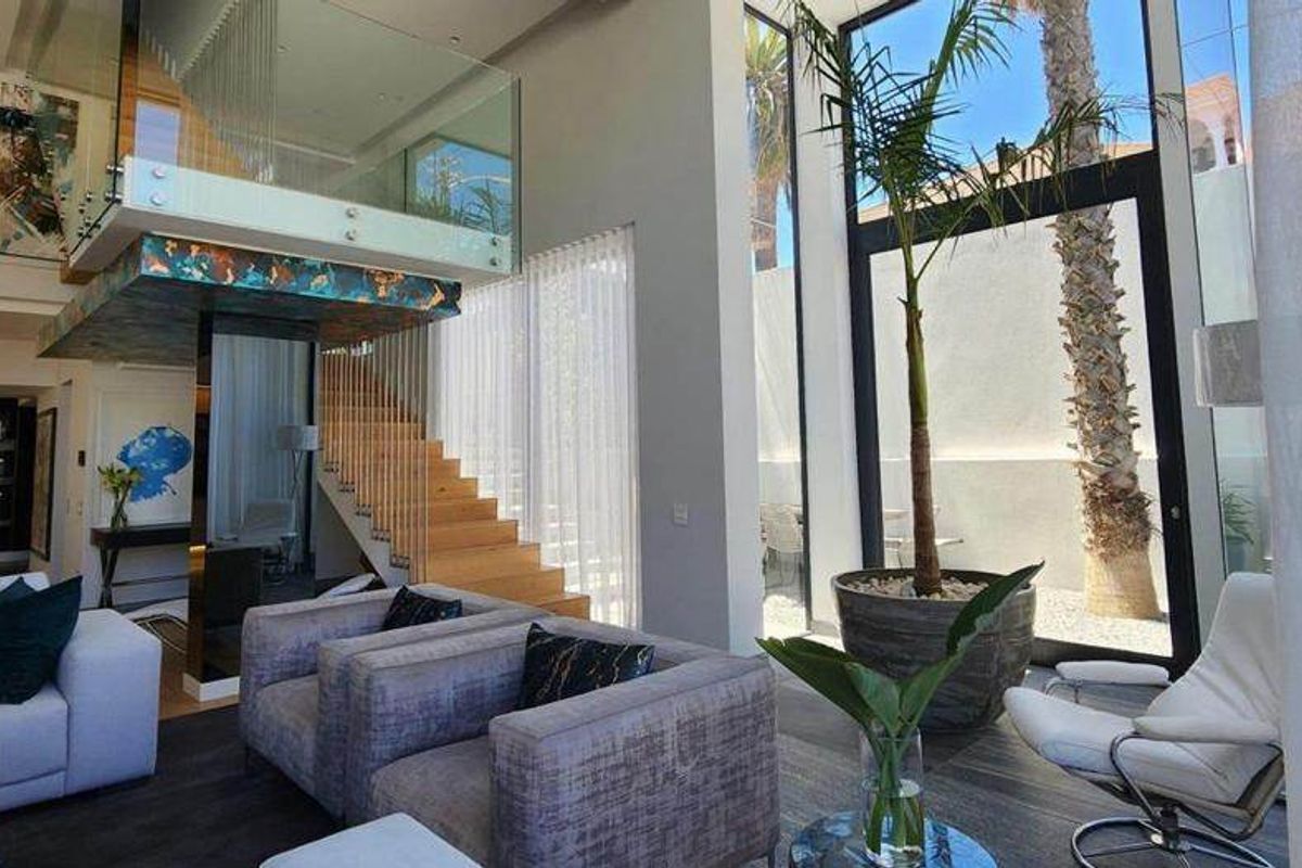 Spacious double-volume living area featuring floor-to-ceiling windows, a modern timber staircase with glass balustrade, and seamless access to the outdoor area.