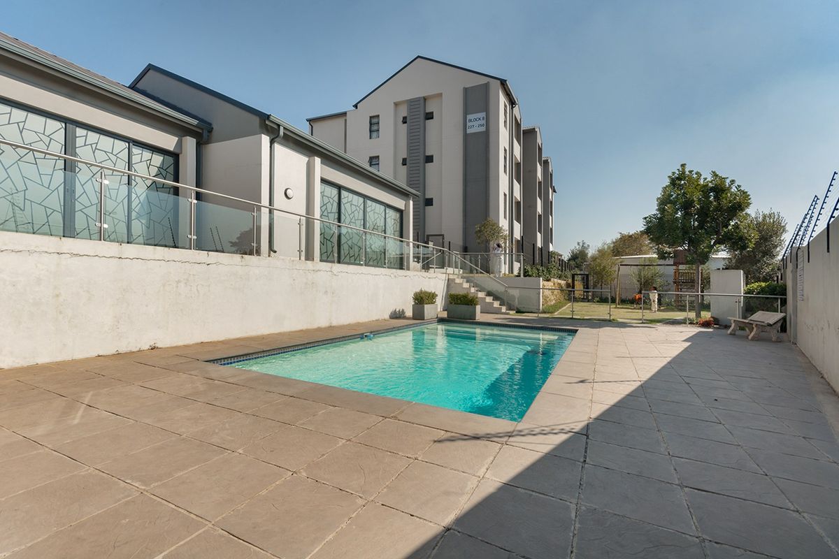 Communal swimming pool area featuring a paved deck, glass balustrades, and secure perimeter fencing within the apartment complex.