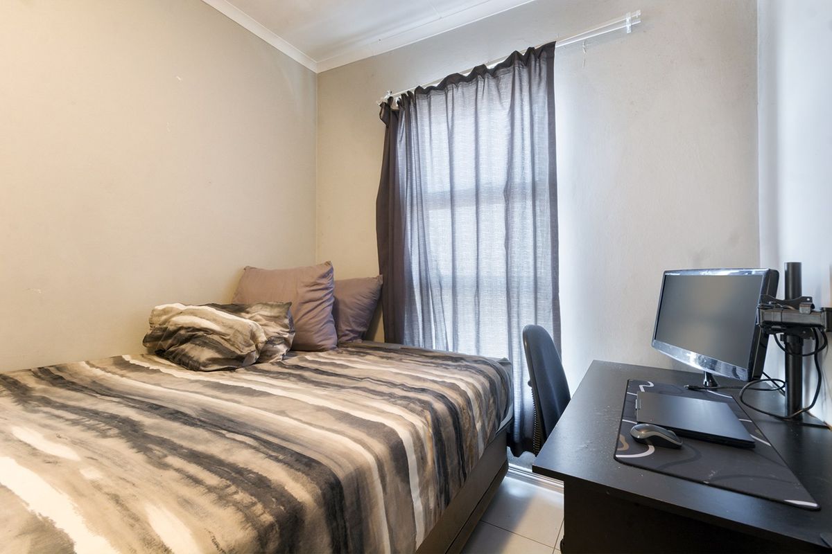 A compact bedroom featuring tiled flooring and a window with a fitted curtain rod, offering a functional space for rest or study.